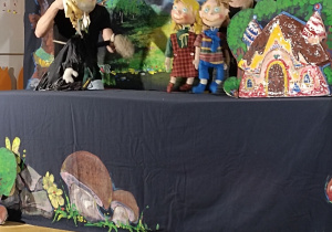 Scenografia przedstawiająca las aktorzy trzymają kukły jasia małgosi i ich taty