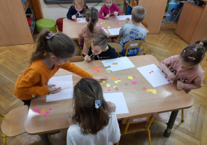 Dzieci siedzą przy stoliku przekładają papierki za pomocą słomek