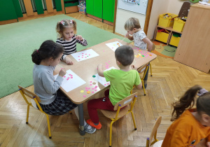 Dzieci siedzą przy stoliku przekładają papierki za pomocą słomek