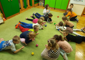 Dzieci leżą na dywanie na brzuchu dmuchają przez słomki na piłeczki