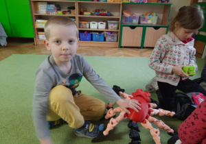 Dwoje dzieci trzyma dużego pająka wydrukowanego na drukarce 3D