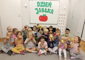 dzieci siedzą przed tablicą z napisem dzień jabłka