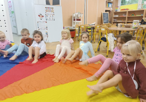 Dzieci siedzą na kolorowej chuście bez skarpetek