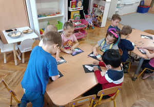 dzieci siedzą przy stoliku odrysowują motyla na czarnym tle
