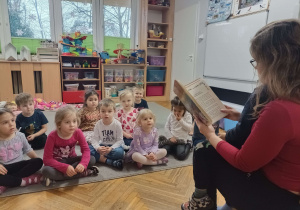 dzieci słuchają bajki czytanej przez kobietę trzymającą chłopca na kolanach
