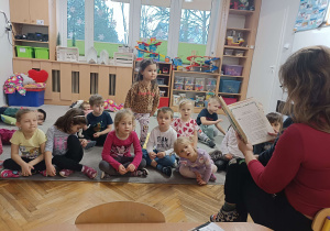 dzieci słuchają bajki czytanej przez kobietę trzymającą chłopca na kolanach