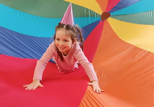 dziewczynka w czapeczce urodzinowej siedzi na kolorowej chuście