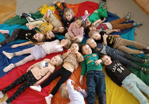 dzieci leżą na kolorowej chuście tworząc koło