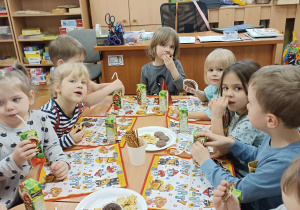 dzieci siedzą przy wspólnym długim stole zastawionym słodyczami