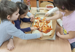 dzieci siedzą przy stolikach układają warzywa wędlinę i ser na cieście od pizzy