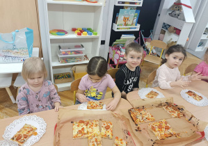 dzieci siedzą przy stolikach i jedzą pizzę