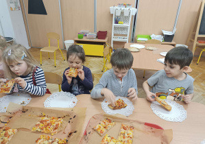 dzieci siedzą przy stolikach i jedzą pizzę