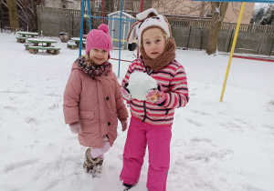 dwie dziewczynki stoją na śniegu jedna trzyma kulę śniegu