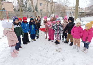 dzieci stoją na śniegu przed nimi stoi bałwan ze śniegu