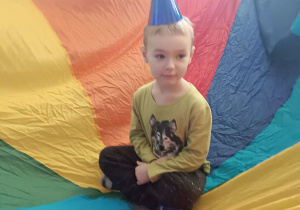 chłopiec w czapeczce urodzinowej siedzi na kolorowej chuście