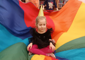 dziewczynka siedzi na kolorowej chuście w urodzinowej czapeczce