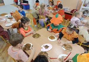 dzieci ubrane w kolory jesieni malują przy stolikach misie