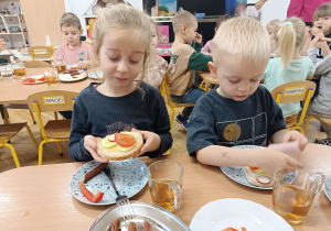 dzieci przy stoliku maja przed sobą na talerzykach kanapki z dużą ilością warzyw