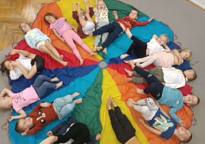 dzieci siedzą bez skarpetek w kole na kolorowej chuście