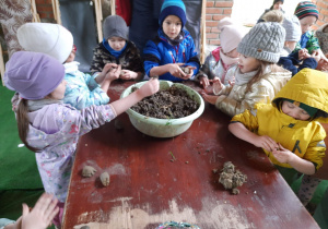 dzieci stoją dookoła stolika lepią kule z gliny