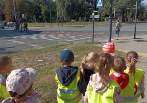 dzieci ubrane w kamizelki odblaskowe idą parami po chodniku