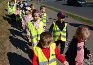 dzieci ubrane w kamizelki odblaskowe idą parami po chodniku