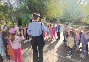 dzieci stoją w kole na chodniku dookoła pani w kwiatowym wianku