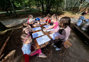 dzieci siedzą przy stoliku w otoczeniu drzew