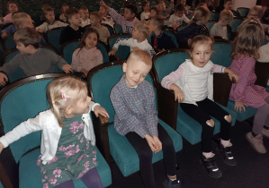 dzieci siedzą na fotelach widowni w teatrze