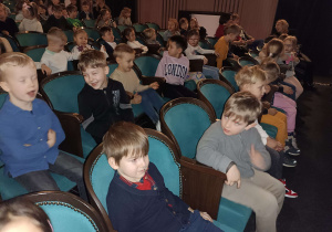 dzieci siedzą na fotelach widowni w teatrze
