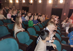 dzieci siedzą na fotelach widowni w teatrze