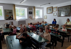 dzieci siedzą w starodawnych ławkach szkolnych
