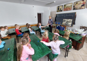 dzieci siedzą w starodawnych ławkach szkolnych