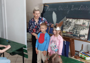 dwoje dzieci stoi obok kobiety chłopiec ma zawieszony na szyji język a dziewczynka ma na głowie ośle uszy