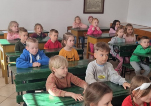 dzieci siedzą w starodawnych ławkach szkolnych