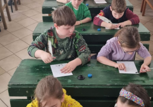 dzieci siedzą w starodawnych ławkach szkolnych