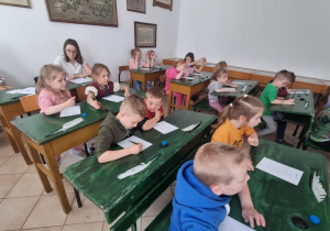 dzieci siedzą w starodawnych ławkach szkolnych
