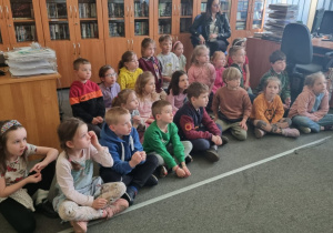 dzieci siedzą na dywanie przed regałem z książkami