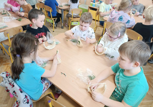 dzieci przy stolikach tworzą małe koszyczki z sizalu