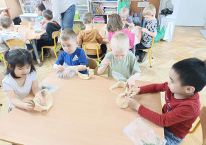 dzieci przy stolikach tworzą małe koszyczki z sizalu