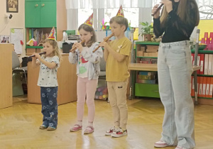 pani z trojgiem dzieci w czapeczkach urodzinowych gra na flecie