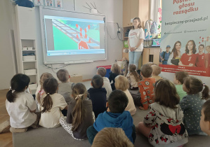 dzieci siedzą przed tablicą multimedialną na której jest znak świętego andrzeja