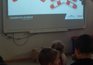 dzieci siedzą przed tablicą multimedialną ze znakami świętego andrzeja
